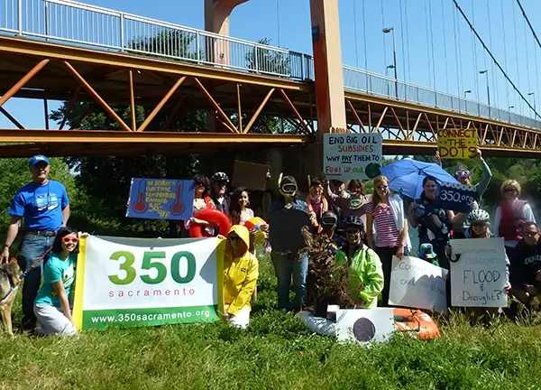 A group of volunteers under the Guy West bridge holding 350 Sacramento and other signs. (Photo attributed to 350 Sacramento.)