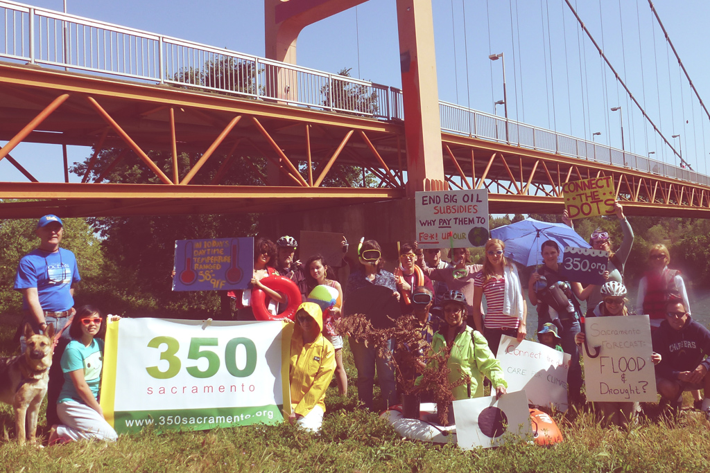 A group of volunteers under the Guy West bridge holding 350 Sacramento and other signs. (Photo attributed to 350 Sacramento)