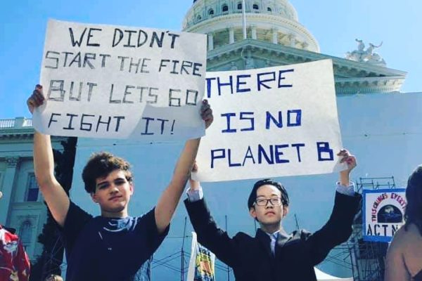 Two young people standing with "No Planet B" signs in front of the Capitol building