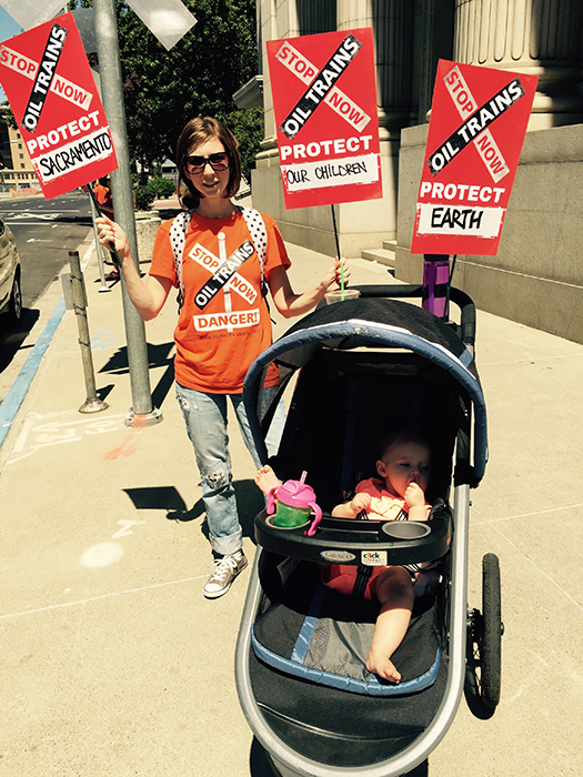 woman with child in stroller, holding signs to protest oil trains